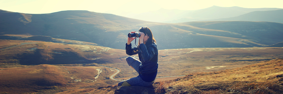 A woman sitting on a hill with binoculars