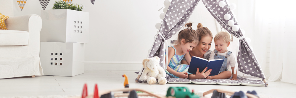 Au pair with host kids reading a book in a tent