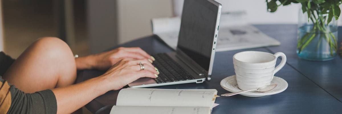 Junge Frau sitzt am Tisch und schreibt an ihrem Laptop