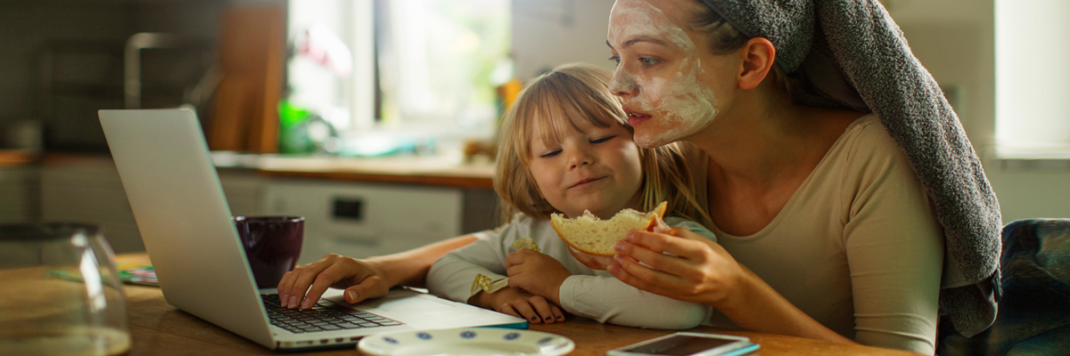 A mother copes with everyday stress - at the kitchen table with a child on her lap, looking at her laptop