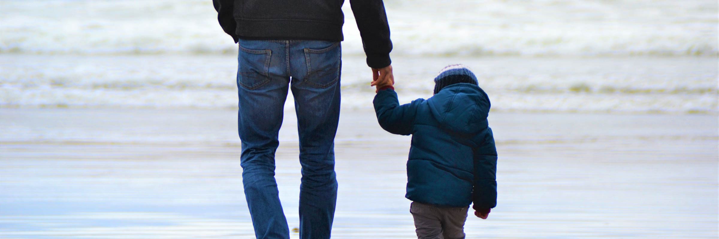 Un padre de la mano con su hijo por la playa