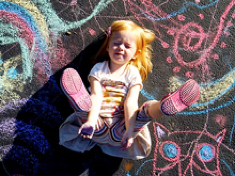 A little girl plays with chalk on the street