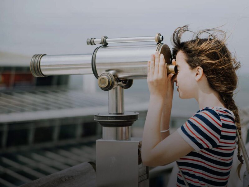 Una ragazza osserva il paesaggio attraverso un telescopio