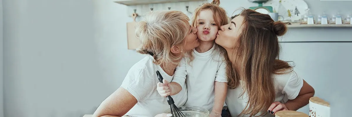A mother and a grandmother kiss the child who sits between them