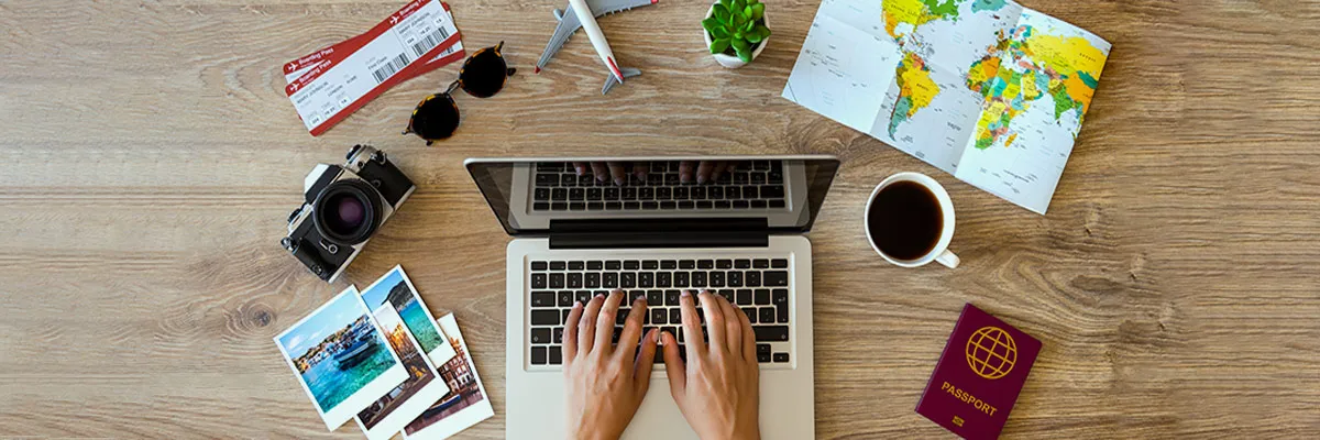 Travel search on a laptop surrounded by travel paraphernalia - camera, tickets, maps etc.