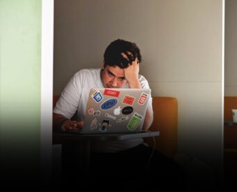 Young man sits in front of laptop looking exasperated