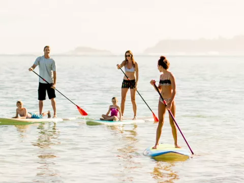 The host family and their au pair enjoying time together while doing stand up paddling