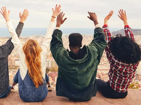 Five people sit in a row on a hill with a view of a city