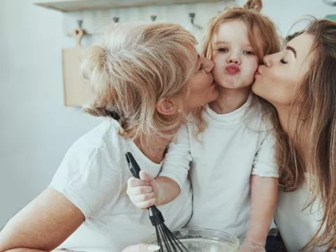 A mother and a grandmother kiss the child who sits between them