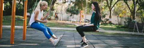 Two young women sitting on swings at a playground