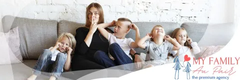 An au pair sits on a sofa with children