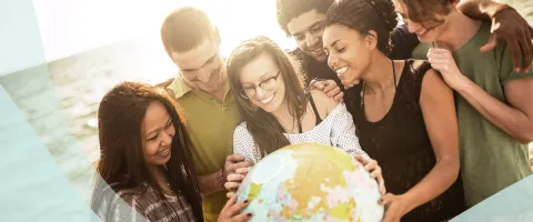 A group of diverse people smiling and holding a globe outdoors.