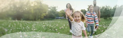 Family walking in a sunny park, child waving.