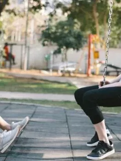 Two young women sitting on swings at a playground